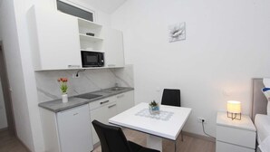 A compact kitchen with white cabinetry, a microwave, and a small dining table with a chair. - SUNNY Studio Apartment (Rovinj)