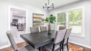 A dining area with a dark wooden table, six upholstered chairs, a potted plant, and a modern chandelier. - Urban Cowboy  (Fort Worth)
