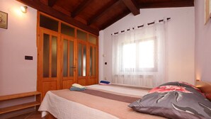 A bedroom with a bed, wooden wardrobe, and a window with sheer curtains.