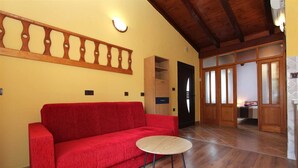 A red sofa and a small round table in a room with wooden flooring and a wooden ceiling.