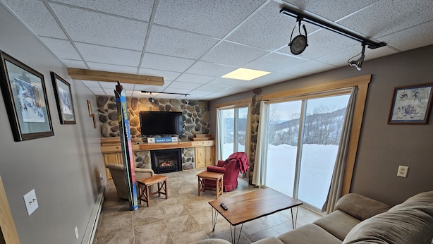 Een gezellige woonkamer met een stenen open haard, een televisie en een groot raam met uitzicht op een besneeuwd landschap.