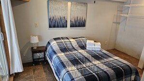 Een opgemaakt bed met een geruit sprei, een bedlampje en twee aan de muur hangende schilderijen.