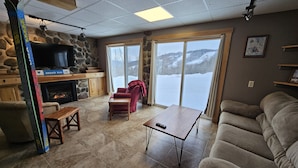 Een gezellige woonkamer met een stenen openhaard, een rode fauteuil, een bank en een groot raam met uitzicht op sneeuw.