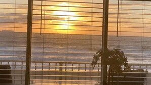 A view through a window with horizontal blinds, overlooking a body of water and a distant shoreline. - Ocean Front Studio on Boardwalk (Virginia Beach)