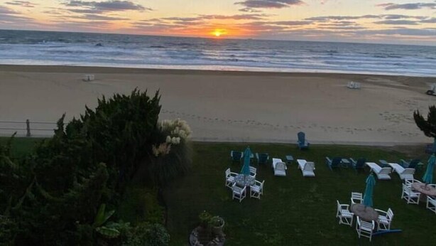 A beach with a sunset view, outdoor seating, and a grassy area with umbrellas. - Ocean Front Studio on Boardwalk (Virginia Beach)
