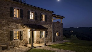 A stone building with a covered porch, a small garden, and a view of the hills in the background. - Villa Bolara (Istria - Grožnjan) (Grožnjan)