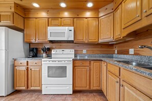 A kitchen with wooden cabinets, a white microwave, a stove, and a granite countertop.