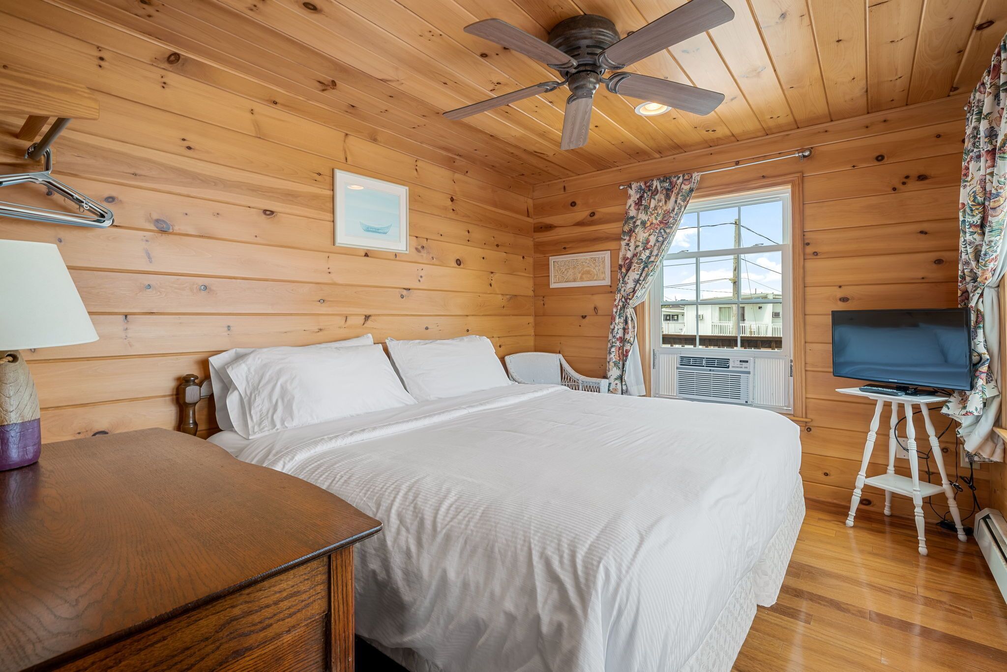 Een slaapkamer in een houten hutje, met een bed, bureau, plafondventilator en televisie.