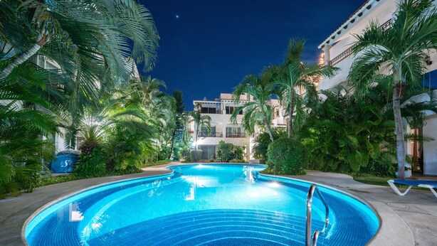 A swimming pool surrounded by palm trees and a building in the background. - Condo Gaviota - Tropical Oasis (Playa del Carmen)
