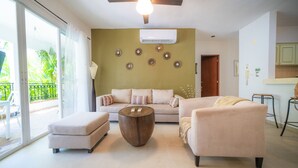 A living room with a sofa, ottoman, and coffee table, a ceiling fan, and an air conditioning unit. - Condo Gaviota - Tropical Oasis (Playa del Carmen)