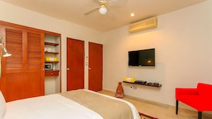 A hotel room with a bed, a red chair, a TV, and a wardrobe. - Condo Gaviota - Tropical Oasis (Playa del Carmen)