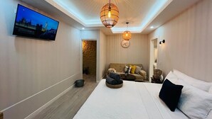 Une chambre moderne avec un grand lit, un téléviseur fixé au mur et deux lampes suspendues.