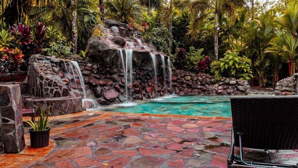 A tropical garden with a waterfall, a pool, and a stone patio. - Cabin Featuring Jacuzzi and Pool in La Fortuna (La Fortuna)