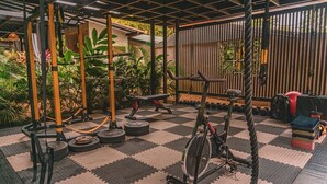 A gym with a variety of equipment including a pull-up bar, weight plates, and a stationary bike. - Cabin Featuring Jacuzzi and Pool in La Fortuna (La Fortuna)