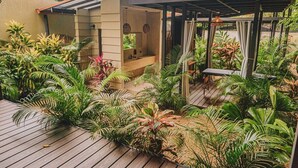 A covered outdoor area with a wooden deck, surrounded by various tropical plants and a small seating area. - Cabin Featuring Jacuzzi and Pool in La Fortuna (La Fortuna)
