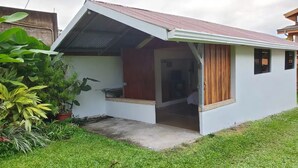 A small, single-story house with a sloped roof, a porch with a wooden railing, and a concrete pathway leading to the entrance.