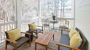 A covered porch with wooden furniture, a ceiling fan, and a view of trees and houses.