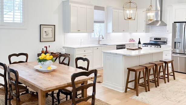 A spacious kitchen with white cabinetry, a wooden dining table, and a large island with stools.