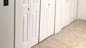 Ein Flur mit drei weißen Türen, einem Lichtschalter an der Wand und beige farbenen Fliesen.