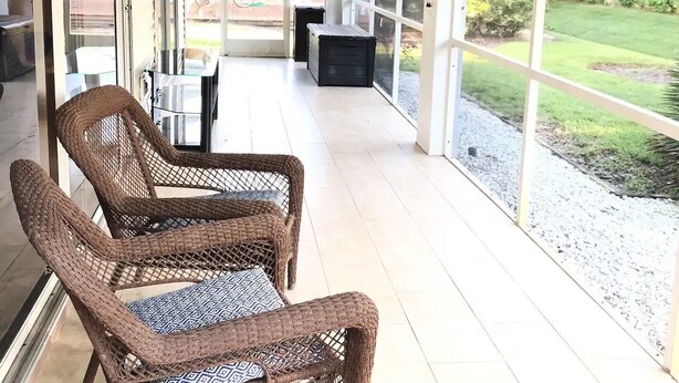 Eine überdachte Terrasse mit Korbmöbeln, einem Deckenventilator und Blick auf den Garten.