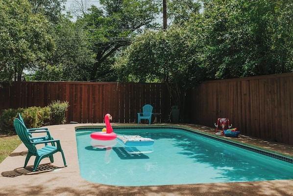 A swimming pool with a wooden fence, a flamingo float, and a blue chair.