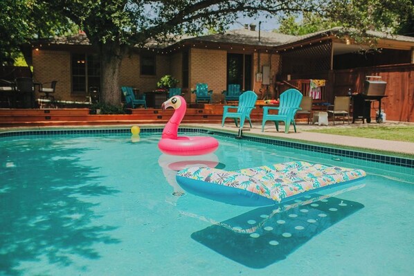 A swimming pool with a pink flamingo float and a floral lounge chair. - Historic Sayles Ranch- Huge Deck + Pool! (Abilene)