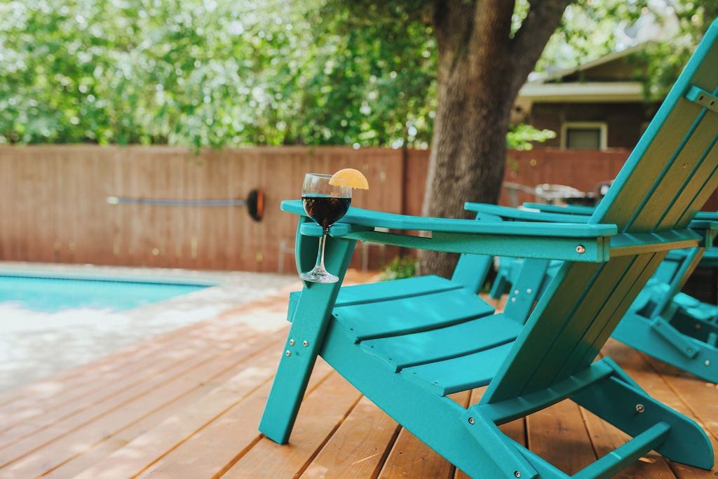 Zona de piscina con terraza de madera, una silla de descanso turquesa y un vaso de bebida oscura con una rodaja de limón.