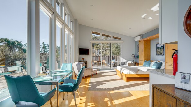Una sala moderna con una mesa de comedor de vidrio, sillas color turquesa, un sofá y una cama.