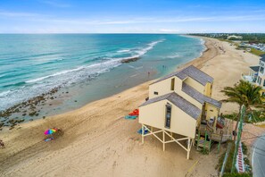 A beach with a lifeguard tower, beach umbrellas, and a sandy shoreline. - The Resort at Bathtub Beach: 19BR/11BA Ocean2River, Pool, Elevator, Dock, Beach! (Stuart)
