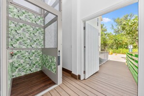A wooden deck leading to a white door with a green leaf pattern, a clear sky, and a green fence. - The Resort at Bathtub Beach: 19BR/11BA Ocean2River, Pool, Elevator, Dock, Beach! (Stuart)
