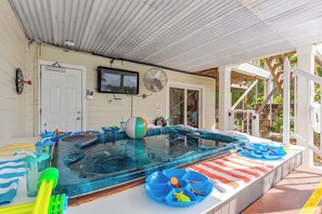Ein überdachter Außenpool mit Whirlpool, einer Tür, einem Ventilator und einem an der Wand montierten Fernseher.