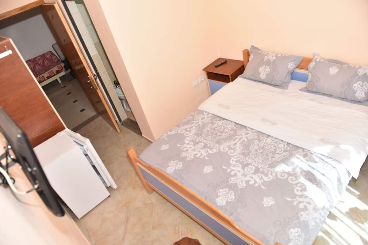 A bedroom with a bed, a nightstand, a wardrobe, and a small white appliance.