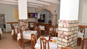 Een restaurant met meerdere ronde tafels en stoelen, een aan de muur bevestigde televisie en een met baksteen beklede open haard.