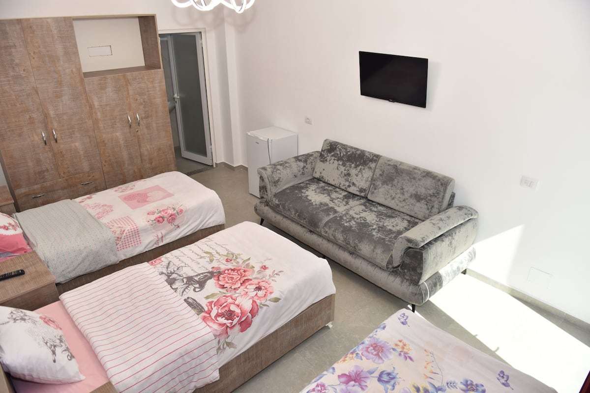 A bedroom with two beds, a grey sofa, a TV, and a wardrobe.