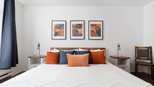 A neatly arranged bedroom with a large bed, multiple pillows, bedside tables, and three framed artworks on the wall.