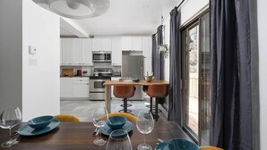 Una cucina moderna con mobili bianchi, elettrodomestici in acciaio inossidabile e una zona pranzo con tavolo in legno e sedie gialle.