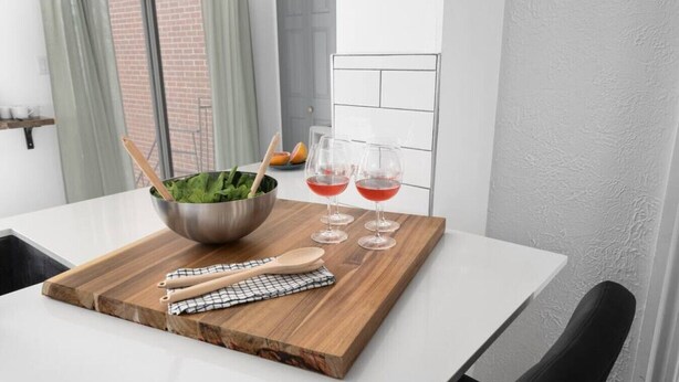A dining table with a wooden board, a metal bowl with greens, two wine glasses, and wooden utensils. - Unique Old, Montreal Patio & Paid Parking 10 Guest (Montréal)