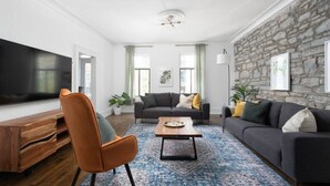A modern living room with a large flat-screen TV, two sofas, a coffee table, and a stone wall. - Unique Old, Montreal Patio & Paid Parking 10 Guest (Montréal)