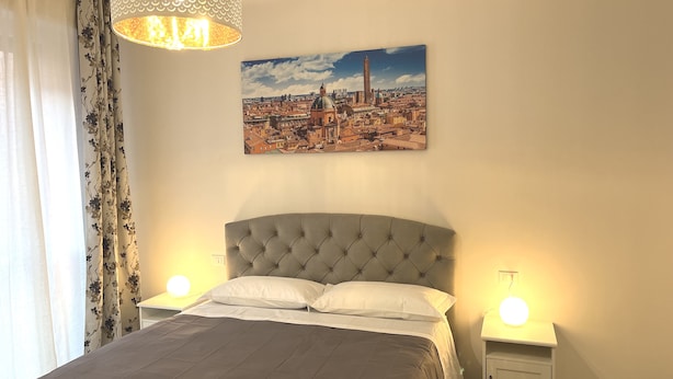 Un dormitorio con una cama grande, dos mesitas de noche, una lámpara colgante y un cuadro de paisaje urbano en la pared.