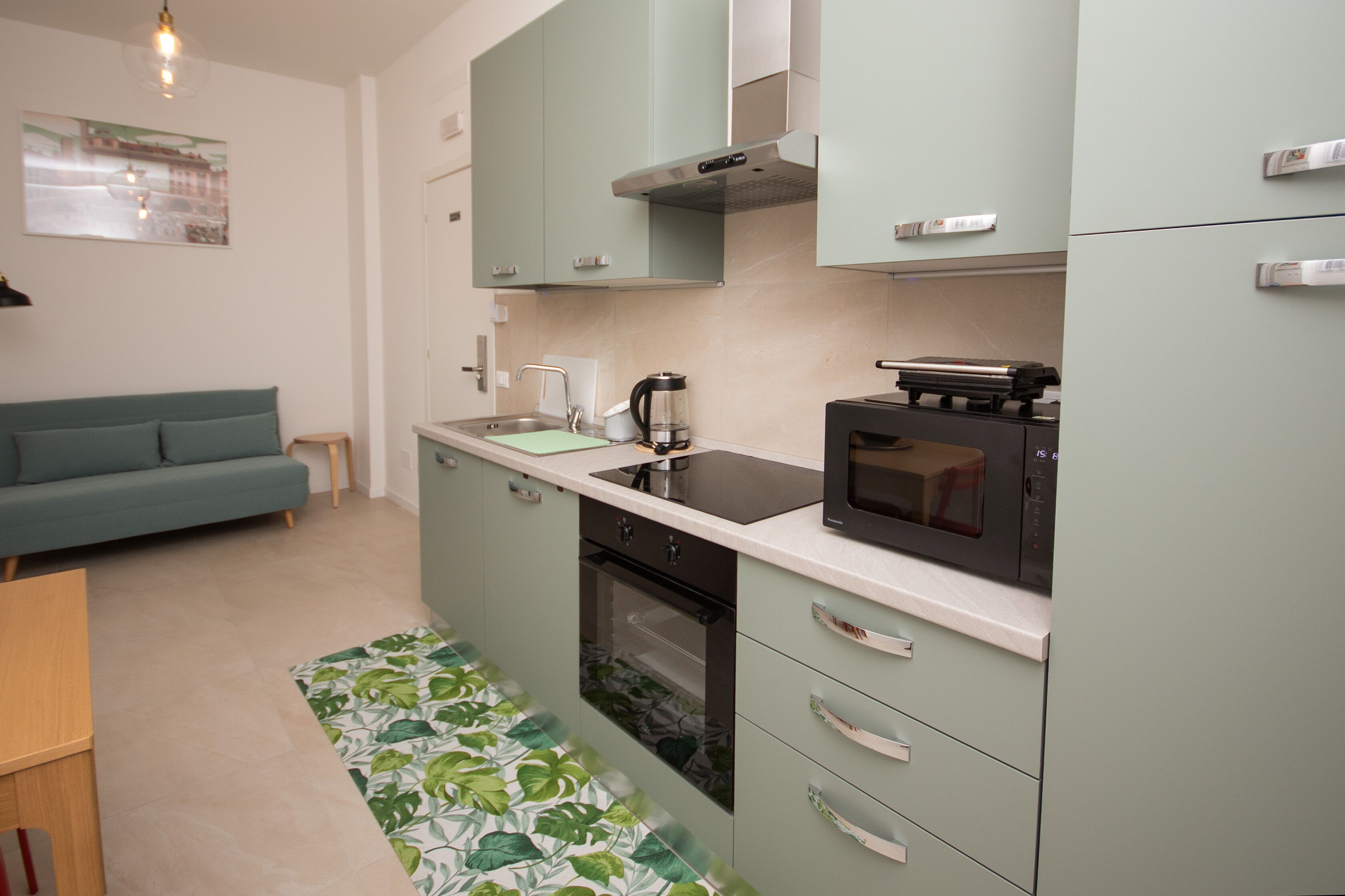 A compact kitchen with a microwave, oven, and sink. There is a green sofa in the adjacent living area.