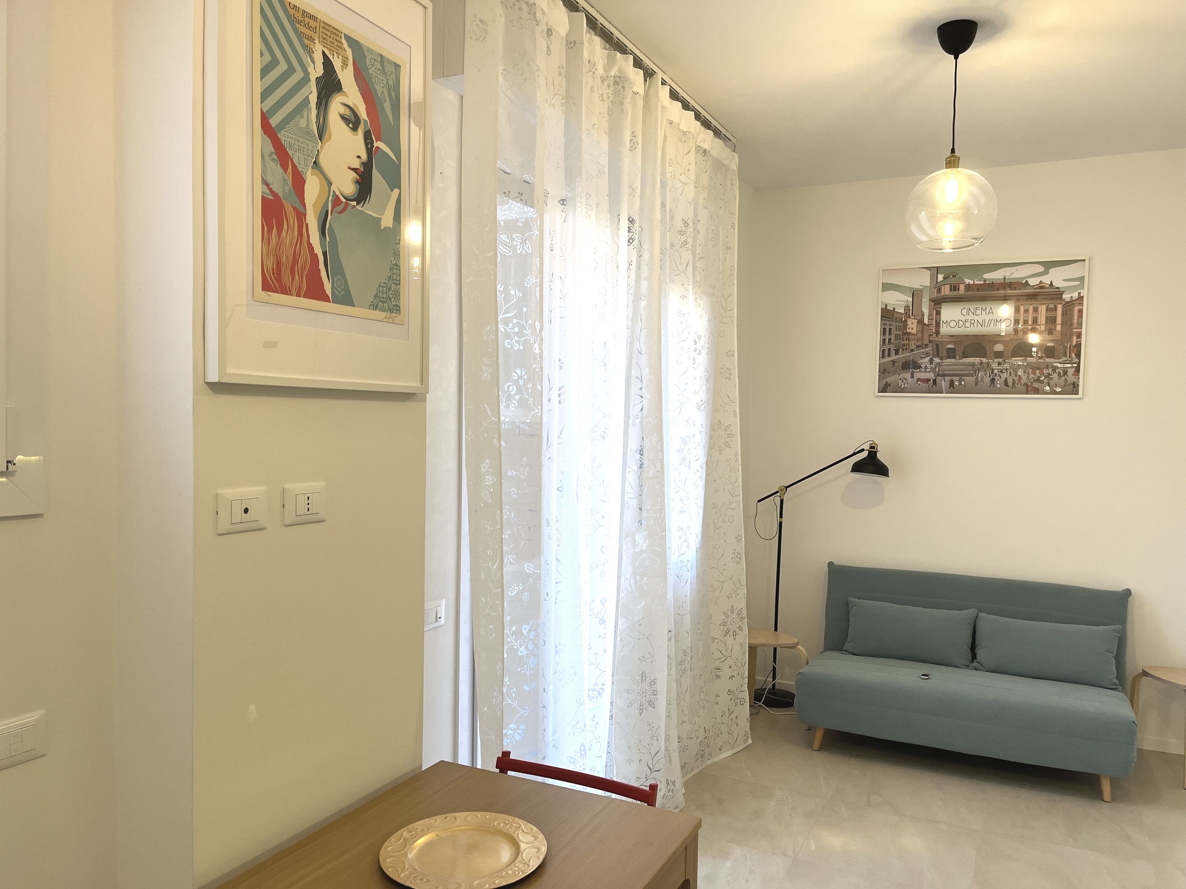 A living room with a blue sofa, a dining table with a plate, a framed picture, a lamp, and a ceiling light.