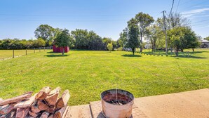 A grassy field with a metal bucket and wood logs in the foreground, surrounded by trees and a fence. - 7 Mi to Depot District: Pet-Friendly w/ Fire Pit (Richmond)