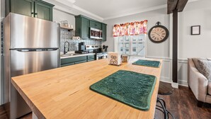 Eine moderne Küche mit grünen Schränken, einem Edelstahl-Kühlschrank und einer Holztischinsel mit grünen Platzsets.