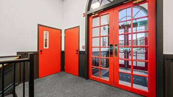 A hallway with red doors and a black railing.