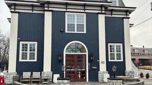 Ein zweistöckiges Gebäude mit dunkelblauer Fassade, einem zentralen Rundbogenportal und der Hausnummer 43 an der Wand.