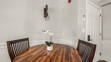 A round wooden dining table with four chairs, a white orchid in a pot, and a wall-mounted decorative piece.