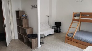 Quarto compacto com beliche, escrivaninha com computador, estante de livros e televisão na parede.