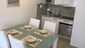 A dining area with a glass table, white chairs, and a kitchen with white cabinets and stainless steel appliances.