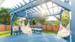 A blue wooden deck with hanging hammocks and a bench.