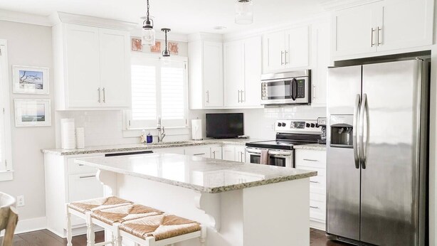 Una cocina moderna con armarios blancos, electrodomésticos de acero inoxidable y una isla central con taburetes de bar.